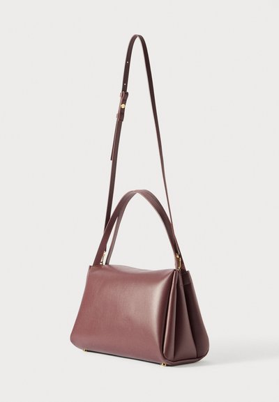 Tmavě fialová kožená kabelka se strukturovaným dnem, krátkými dvojitými uchy a dlouhým nastavitelným ramenním popruhem na jednobarevném pozadí.