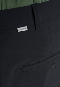 Black trousers with a smooth, matte texture, featuring a back pocket and a small Houdini label on the waistband for branding.