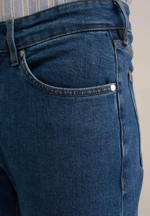 Jeans iz denima v temno modri barvi z gladko teksturo, ki vključujejo sprednji žep, kovinske gumbe in kontrastno šivanje vzdolž šivov.