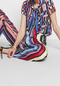 Tenue colorée composée d'un haut à manches courtes et d'un pantalon rayé dans des tonalités de bleu, rouge et jaune, fabriquée en tissu léger avec une coupe décontractée.