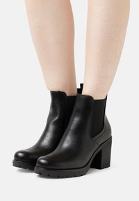 Schwarze Leder-Stiefeletten mit einem dicken Absatz und elastischen Seitenpaneelen. Glatte Textur mit einer abgerundeten Spitze und profiliertem Sohlen für besseren Halt.