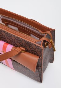 Brun bag med mønster og struktureret design, der har en lynlåslukning, læderdetaljer, og en frontlomme med pink og røde striber.