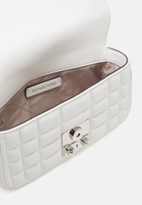 Vitt vadderat läderhandtag med silverdetaljer. Insidan är klädd med ett brunt tyg och har en sidetikett präglad med "Michael Kors."