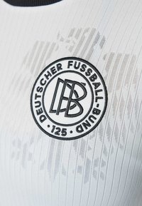 Synthetic white jersey with ribbed texture; features a black embroidered round logo with "DEUTSCHER FUSSBALL-BUND" and "125."