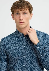 Camicia button-up blu navy con motivo a foglie bianche, dotata di colletto aperto e bottoni tondi, con una superficie di tessuto liscia.