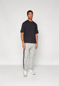 Juodas trumpomis rankovėmis marškinėlių ir pilkų sportinių kelnių su juodomis šoninėmis juostelėmis derinys. Medžiaga atrodo minkšta, o siluetas laisvas.