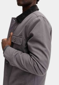 Grå lærredskajak med en kordfløjlskrave, der har en brystlomme med knap og teksturerede strikmanchetter. Skræddersyet pasform med en struktureret design.