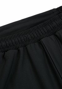 Pantalons noirs avec une taille élastique, présentant une texture lisse et une coupe ample. Le tissu est léger et s'étire pour plus de confort.