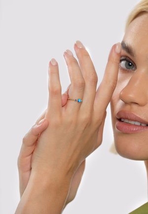 Kultasormus, jossa kolme sinistä jalokiveä, hienovarainen sormus ja kiiltävä viimeistely, esillä kädessä, jonka kynnet ovat huolitellut.