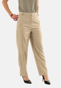 Pantaloni beige su misura con due bottoni frontali, tasche laterali e un taglio dritto. Presentano un tessuto morbido, indossati con tacchi alti neri.