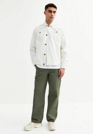Vit knappad jacka med framfickor, kombinerad med olivgröna cargobyxor. Modell iförd krämfärgade sneakers. Enkelt, funktionellt design.
