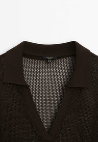 Polo à maille ouverte brun foncé avec un col large et un décolleté en V, montrant la texture et l'étiquette à l'intérieur de l'encolure.