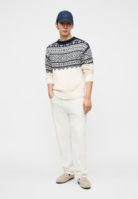 Μπλούζα κρέμα με μοτίβο fair isle σε ναυτικό μπλε, λευκό παντελόνι και μπεζ παπούτσια χωρίς κορδόνια. Συνδυασμένο με καπέλο σε ναυτικό μπλε. Απλό και καθημερινό σύνολο.