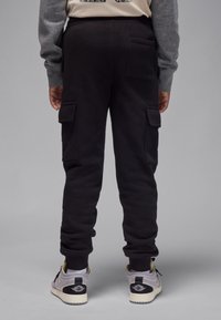 Pantaloni cargo tip polar negri, cu două buzunare laterale, picioare conice și talie elastică. Purtate cu pantofi sport gri deschis și albi.