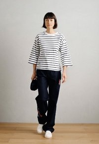 Λευκό και ναυτικό ριγέ υπερμεγέθη πουκάμισο, με φαρδιές μανίκες, συνδυασμένο με σκούρο τζιν που διαθέτει λουλουδάτα κεντήματα και λευκά αθλητικά παπούτσια.