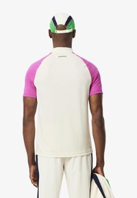 Kortärmad krämfärgad t-shirt med rosa raglanärmar, prydd med en subtil logotyp på baksidan, tillsammans med matchande krämfärgade byxor.