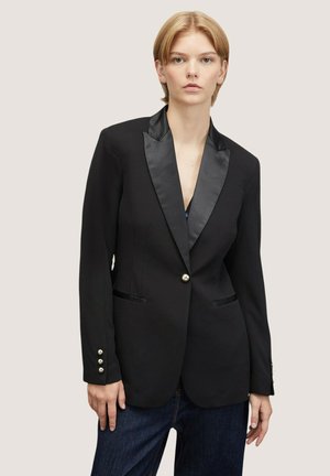 Blazer nero con rever in raso, chiusura a un bottone e due tasche frontali. Presenta polsini a tre bottoni e una vestibilità sartoriale.