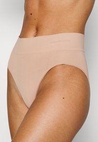 Nackte, nahtlose hochgeschnittene Unterwäsche aus weichem, dehnbarem Stoff mit glatter Oberfläche und unauffälliger Markenkennung am Bund.