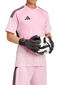 Rosa synthetisches Fußballtrikot mit kurzen Ärmeln, strukturiertem Design und schwarzen Akzenten. Schwarze Handschuhe halten einen schwarz-weißen Fußball.