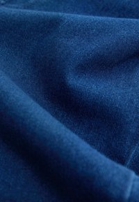 Gros plan sur un tissu bleu foncé lisse avec une texture de tissage fin visible et des plis subtils créant des ombres douces et des reflets.