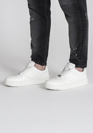 Baskets blanches avec un design texturé, bout arrondi et semelle en caoutchouc plate. Présente un laçage à l'avant et une marque minimale sur la languette.