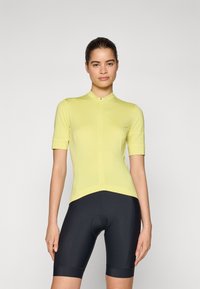 T-skjorte med kort erm for sykling i lys gul, med en frontglidelås, med en tettsittende design og glatt tekstur, kombinert med svarte sykkelshorts.