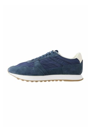 Blauer und marineblauer Sneaker mit weißem Fersenkragen, Veloursleder-Overlays und weißer Sohle mit braunem Profil, von der Seite auf weißem Hintergrund gesehen.