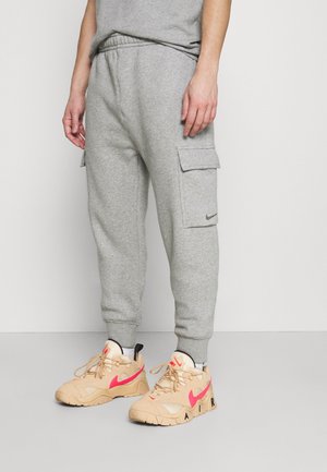 Mand iført lysegrå cargo-joggingbukser med sidelommer og beige Nike-sneakers med lyserøde swoosh-logoer.