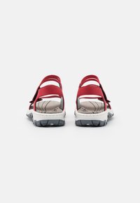 Sandales synthétiques rouges avec des sangles ajustables, semelles intérieures rembourrées et semelles extérieures en caoutchouc noir présentant un motif de traction. Vue arrière.