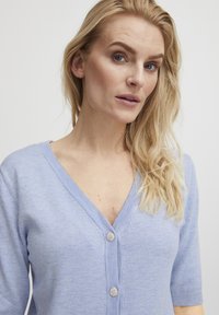 Lichtblauwe V-hals cardigan van zacht materiaal, met korte mouwen en decoratieve zilveren knopen aan de voorkant. Gemakkelijk aanvoelende textuur, casual pasvorm.