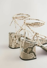 Hohe Sandalen mit Schlangenprint-Design, einem strukturierten beigen und schwarzen Muster, dünnen Riemen und klobigen Blockabsätzen.