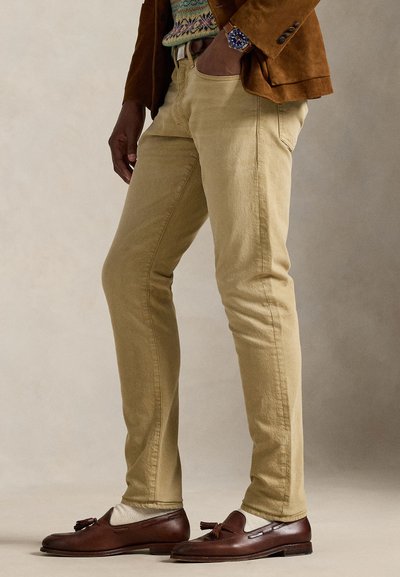 Calças chino de algodão caqui com corte slim, apresentam bolsos frontais, textura subtil, combinadas com mocassins castanho escuro e um suéter estampado.