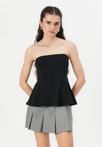 Top peplum senza spalline di colore nero con un corpetto aderente e un orlo svasato, abbinato a una mini gonna plissettata grigia, che mette in mostra un tessuto liscio e linee pulite.