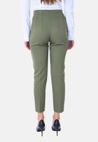 Pantaloni su misura verde oliva a vita alta con cuciture laterali, vestibilità aderente e orli rifiniti. Abbinati a décolleté nere con tacco a spillo.