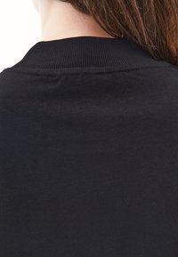 Czarna bawełniana bluza z okrągłym dekoltem, gładka w dotyku o prostym wzorze, przedstawiona z tyłu, z widocznymi włosami sięgającymi ramion.