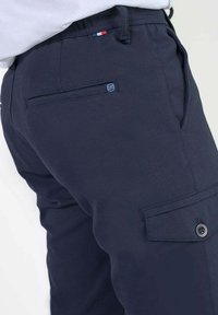 Marineblauwe cargo-broek van getextureerde stof, met een zijzak met knoop, een achterzak en een klein logo dichtbij de tailleband.