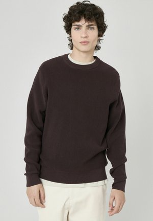 Sweatshirt côtelé de couleur brun foncé avec manches longues et col rond, présentant une texture douce et un subtil bord intérieur contrasté.