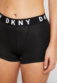 Crne DKNY kratke hlače s bijelim logotipom na pojasu. Mekani materijal, uski kroj, s glatkom teksturom i kratkim nogavicama.