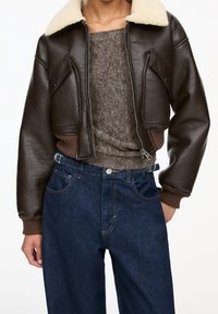 Bruine leren cropped jack met een crèmekleurige schapenvacht kraag, gecombineerd met een grijze gebreide trui en donkerblauwe hoge taille jeans.