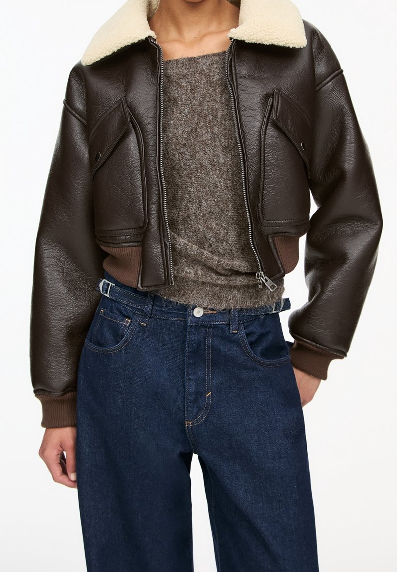 Bruine leren cropped jack met een crèmekleurige schapenvacht kraag, gecombineerd met een grijze gebreide trui en donkerblauwe hoge taille jeans.