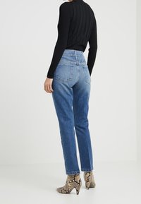 Höga blå jeans med avslappnad passform, fem fickor och en lätt blekning. Matchas med mönstrade klackstövlar och en svart ribbad topp.