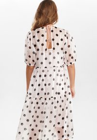 Prickig klänning i durchsiktigt tyg, med ett lager på lager-design, puffärmar och en ryggöppning med snörning.