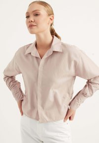 Camicia button-up rosa chiaro a maniche lunghe con colletto, maniche con polsini e orlo leggermente corto. Tessuto morbido.