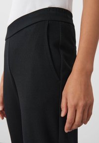 Svarta skräddarsydda byxor med texturerad väv. Har en smal passform, snedställda sidofickor och en slät midjeband för komfort.