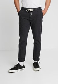 Czarne zwężane spodnie z elastycznym pasem, zawiązywane sznurkiem, z mankietami na końcach nogawek i bocznymi kieszeniami, zestawione z czarnymi trampkami i białymi skarpetkami.