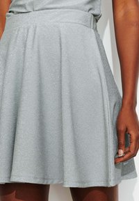 Jupe pailletée argentée en tissu léger avec une coupe évasée. Dotée de plis et d'une ceinture lisse.