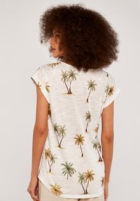 Short-sleeve, white shirt featuring a palm tree print in green and brown. Light, textured fabric with a curved hem.