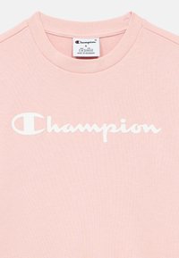 Ρόζ φωτεινό T-shirt Champion με λευκή εκτύπωση λογότυπου στο στήθος και ετικέτα μεγέθους που δείχνει μικρό για ηλικία 7/8, κατασκευασμένο στη Μιανμάρ.