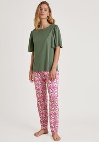 Groen top met korte mouwen en opstaande mouwen, gecombineerd met roze gestreepte broek met bloem- en geometrische patronen in verschillende tinten.