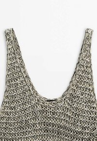 Gros plan sur un haut sans manches en maille avec des larges bretelles en fil beige et noir, présentant un motif texturé à mailles ouvertes.